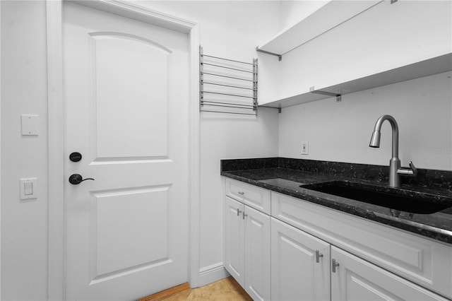 kitchen featuring dark stone countertops, white cabinetry, open shelves, and a sink