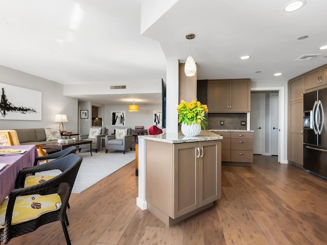 kitchen featuring stainless steel fridge, light hardwood / wood-style flooring, light stone counters, and decorative light fixtures