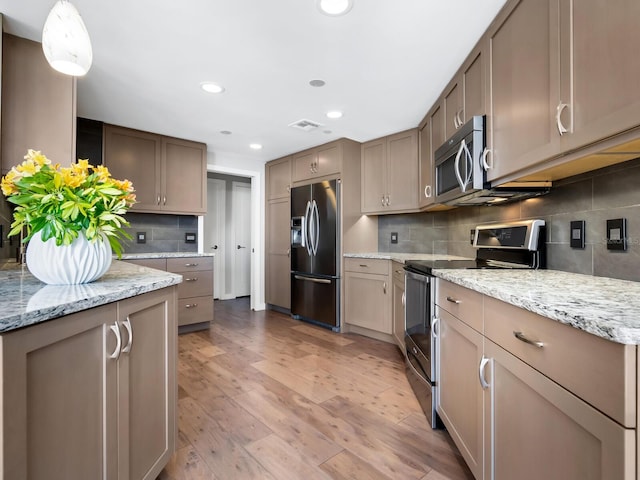 kitchen featuring appliances with stainless steel finishes, light wood-type flooring, tasteful backsplash, light stone counters, and decorative light fixtures