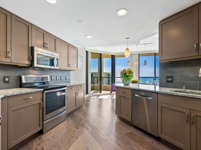 kitchen featuring hanging light fixtures, light stone counters, backsplash, and appliances with stainless steel finishes