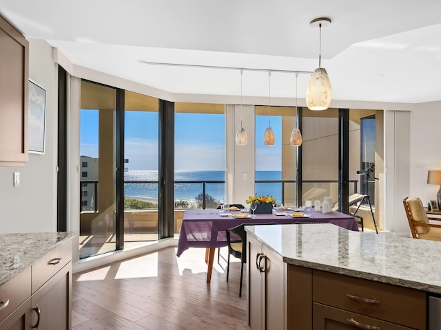 kitchen with light stone countertops, expansive windows, pendant lighting, a water view, and hardwood / wood-style floors