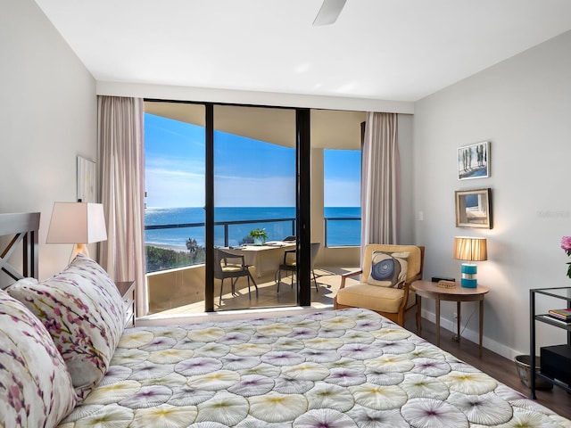 bedroom featuring a wall of windows, ceiling fan, a water view, and hardwood / wood-style flooring