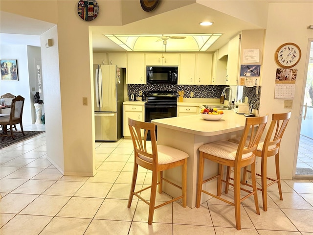 kitchen with a breakfast bar, light tile patterned floors, sink, and black appliances