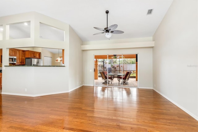 unfurnished living room with ceiling fan, a high ceiling, and light wood-type flooring