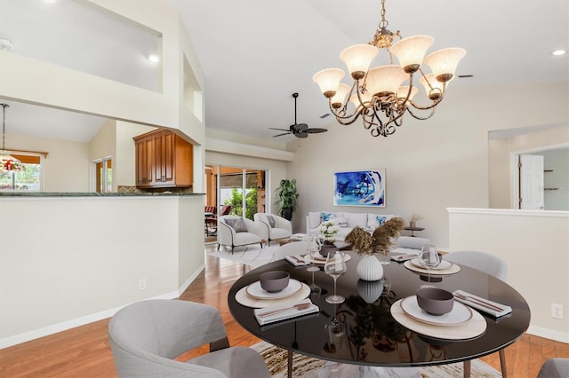 dining space with lofted ceiling, ceiling fan with notable chandelier, and light wood-type flooring