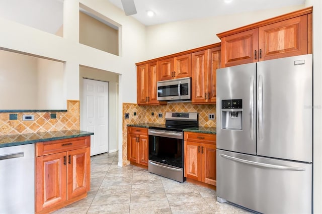 kitchen with high vaulted ceiling, light tile patterned floors, dark stone counters, stainless steel appliances, and decorative backsplash