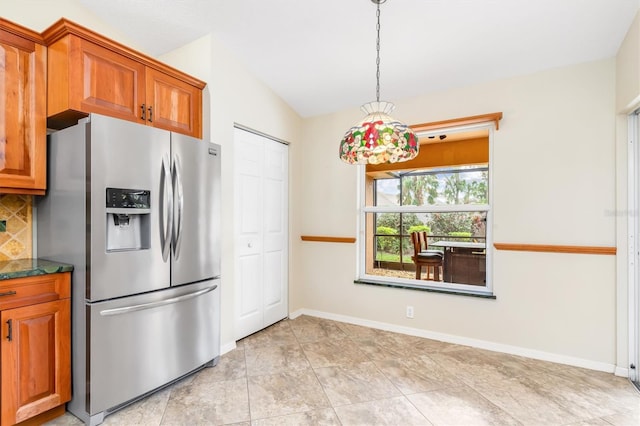 kitchen featuring lofted ceiling, pendant lighting, stainless steel refrigerator with ice dispenser, decorative backsplash, and dark stone counters