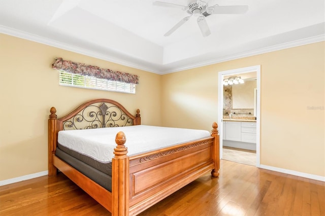 bedroom featuring wood-type flooring, ornamental molding, ceiling fan, a tray ceiling, and ensuite bath