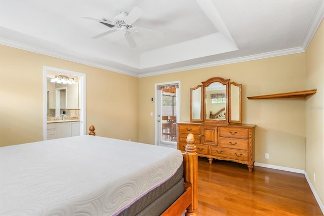 bedroom featuring connected bathroom, hardwood / wood-style flooring, ornamental molding, ceiling fan, and a tray ceiling