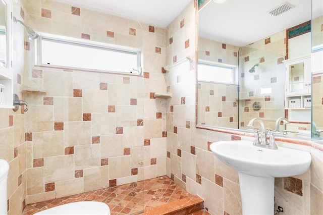 bathroom featuring sink, tiled shower, tile walls, and toilet