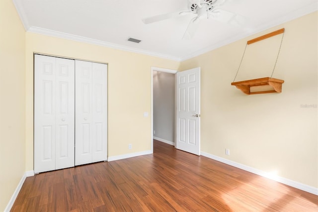 unfurnished bedroom featuring hardwood / wood-style flooring, crown molding, ceiling fan, and a closet