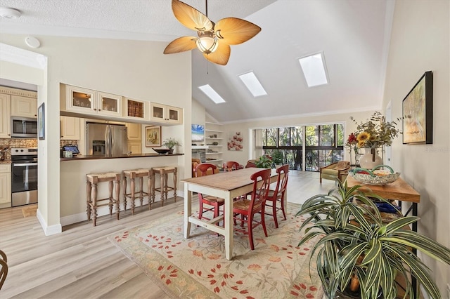 dining area featuring light wood finished floors, crown molding, a skylight, high vaulted ceiling, and a ceiling fan