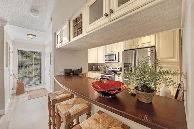 kitchen featuring ornamental molding, a textured ceiling, appliances with stainless steel finishes, a breakfast bar area, and decorative backsplash