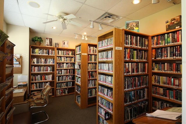 interior space with carpet flooring, bookshelves, a drop ceiling, and ceiling fan