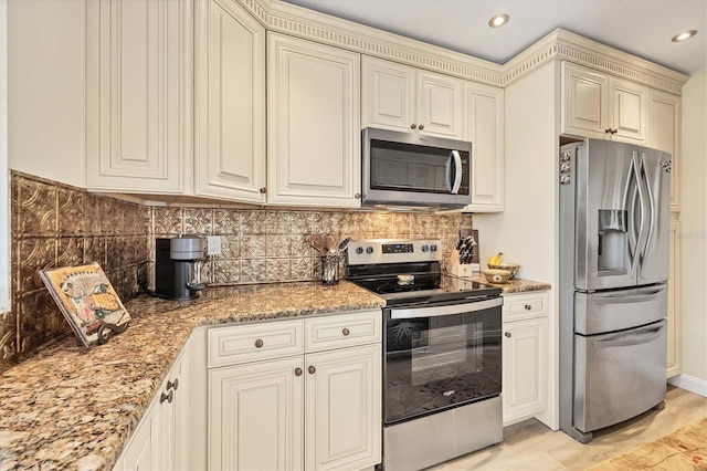 kitchen with light stone counters, backsplash, cream cabinets, and stainless steel appliances