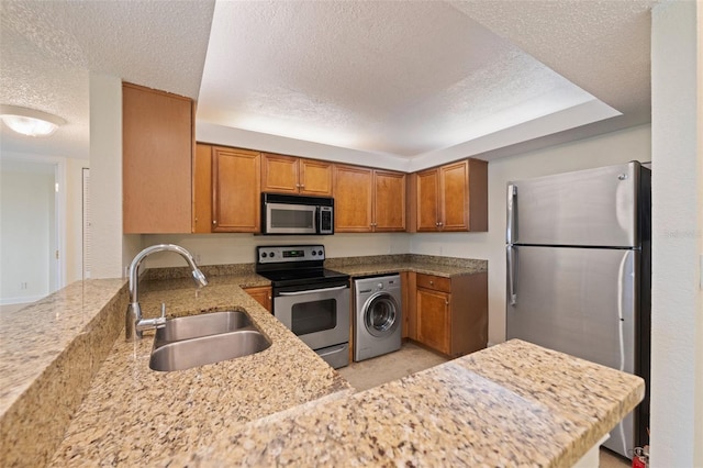 kitchen with sink, kitchen peninsula, a textured ceiling, washer / dryer, and appliances with stainless steel finishes