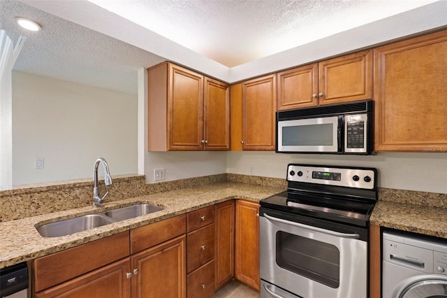 kitchen with light stone countertops, appliances with stainless steel finishes, a textured ceiling, sink, and washer / dryer