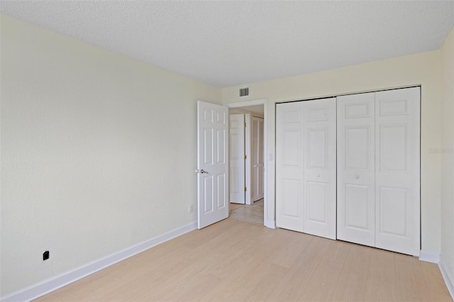 unfurnished bedroom featuring a textured ceiling, light hardwood / wood-style floors, and a closet