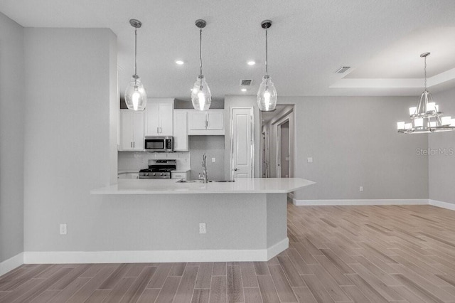 kitchen featuring light wood finished floors, stainless steel appliances, light countertops, white cabinetry, and a sink