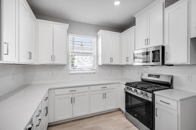 kitchen with stainless steel appliances, light countertops, decorative backsplash, wood tiled floor, and white cabinetry