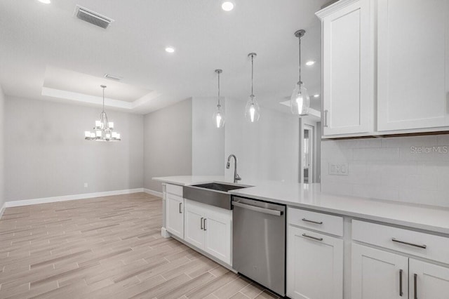 kitchen with a sink, visible vents, light wood-style floors, stainless steel dishwasher, and a tray ceiling