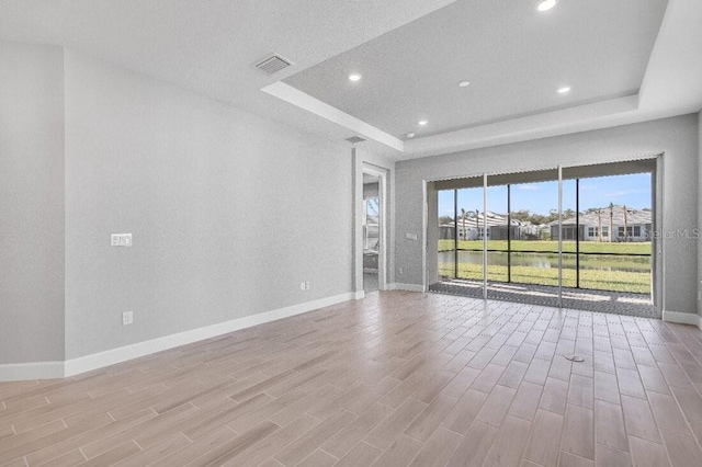 unfurnished living room featuring a tray ceiling, recessed lighting, visible vents, wood finished floors, and baseboards