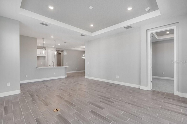 unfurnished living room with a sink, wood finish floors, a raised ceiling, and baseboards