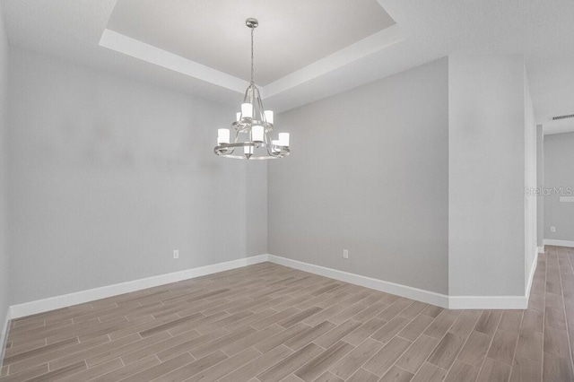 spare room with a chandelier, baseboards, a raised ceiling, and wood finish floors