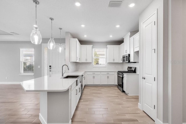 kitchen with a peninsula, light wood finished floors, visible vents, and appliances with stainless steel finishes