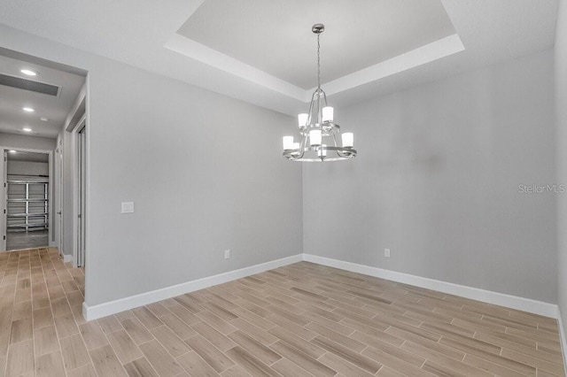 spare room with a chandelier, wood finish floors, visible vents, baseboards, and a raised ceiling