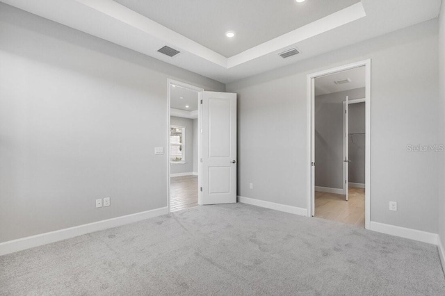 unfurnished bedroom with a tray ceiling, visible vents, and carpet flooring