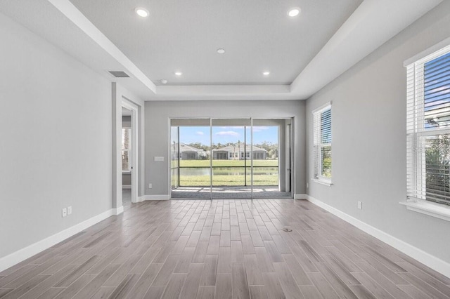 unfurnished room with a tray ceiling, recessed lighting, baseboards, and wood finished floors