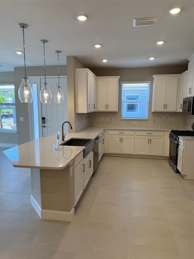 kitchen featuring sink, white cabinetry, stainless steel appliances, light tile patterned flooring, and decorative light fixtures