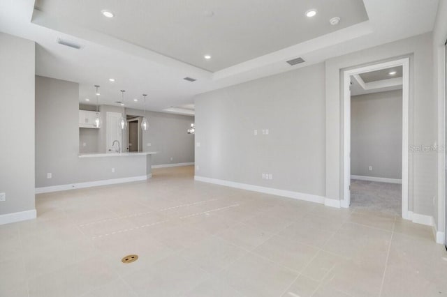 unfurnished living room featuring baseboards, a raised ceiling, visible vents, and recessed lighting