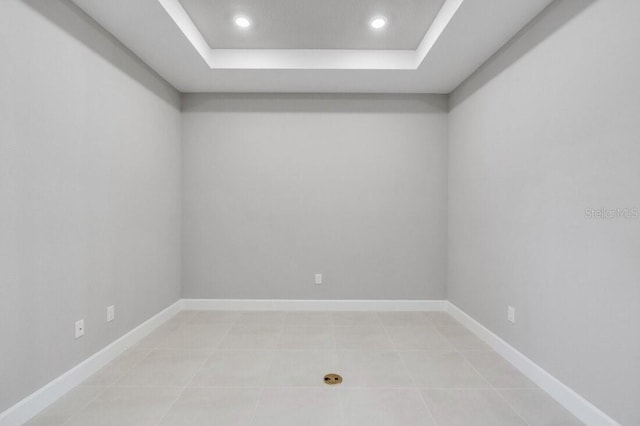 spare room with a tray ceiling, light tile patterned floors, baseboards, and recessed lighting