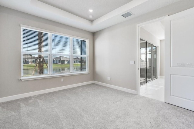 empty room with carpet flooring, a raised ceiling, visible vents, and baseboards