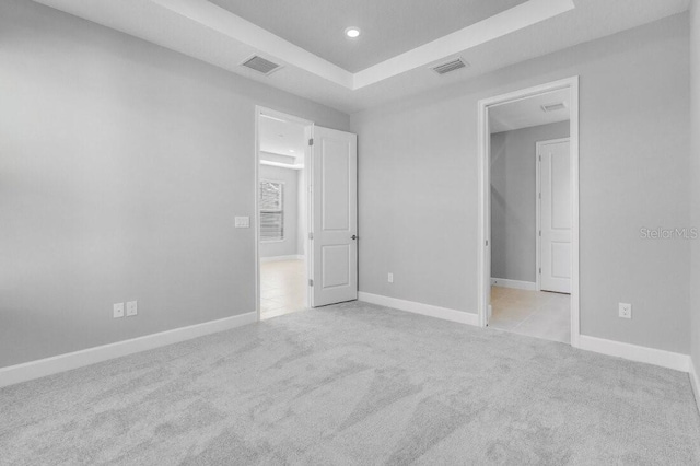 unfurnished bedroom with carpet floors, visible vents, and a tray ceiling