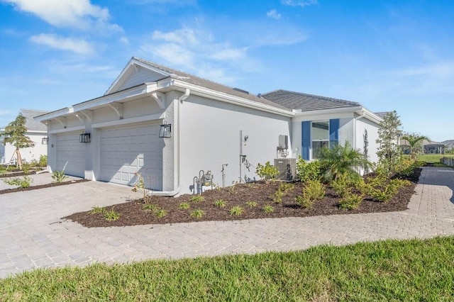 view of property exterior featuring a garage, central air condition unit, decorative driveway, and stucco siding