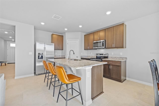 kitchen with sink, stainless steel appliances, light stone counters, a kitchen bar, and a kitchen island with sink