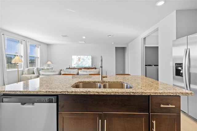 kitchen with light stone countertops, dark brown cabinetry, stainless steel appliances, and sink