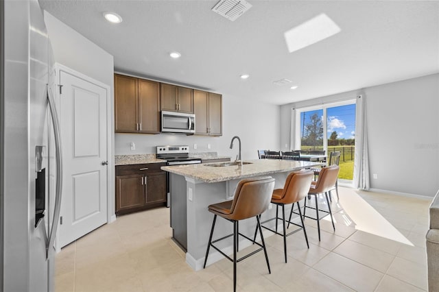 kitchen with light stone countertops, sink, stainless steel appliances, a kitchen breakfast bar, and a center island with sink