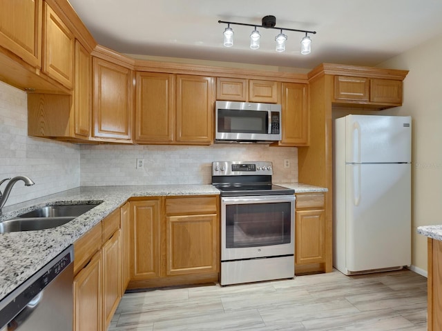 kitchen featuring appliances with stainless steel finishes, backsplash, light stone counters, sink, and light hardwood / wood-style flooring