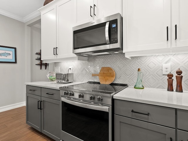 kitchen featuring ornamental molding, gray cabinetry, stainless steel appliances, white cabinets, and light hardwood / wood-style floors