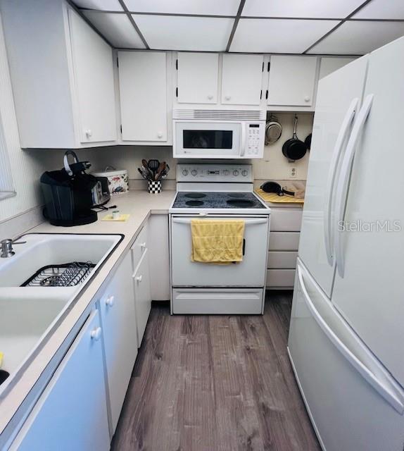 kitchen featuring white cabinetry, a drop ceiling, sink, dark hardwood / wood-style floors, and white appliances