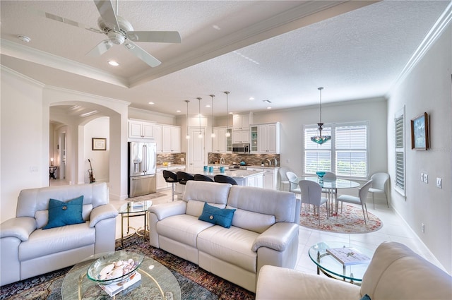 tiled living room with ceiling fan, ornamental molding, and a textured ceiling