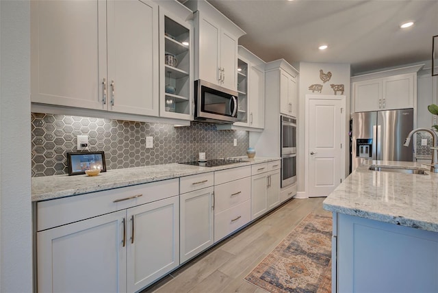 kitchen with white cabinets, sink, light wood-type flooring, light stone counters, and stainless steel appliances