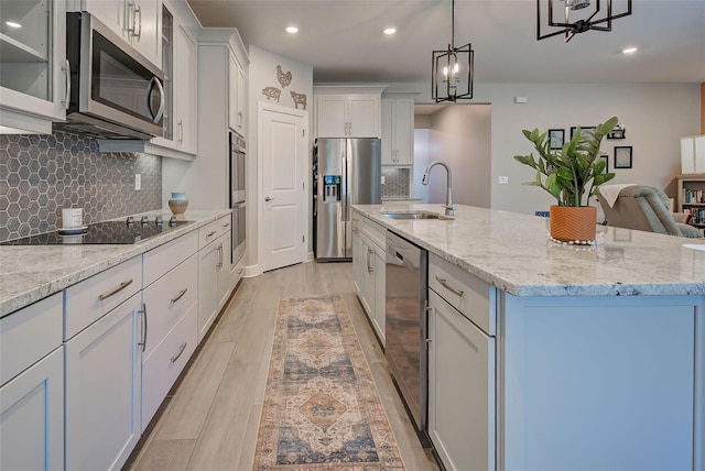 kitchen with stainless steel appliances, sink, a center island with sink, light hardwood / wood-style floors, and hanging light fixtures