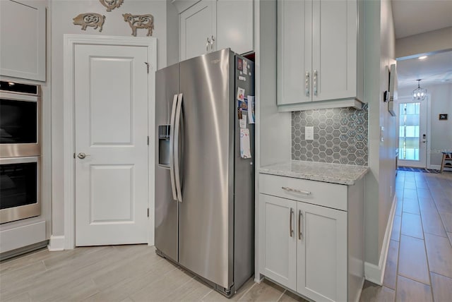 kitchen featuring decorative backsplash, light stone countertops, light wood-type flooring, and appliances with stainless steel finishes