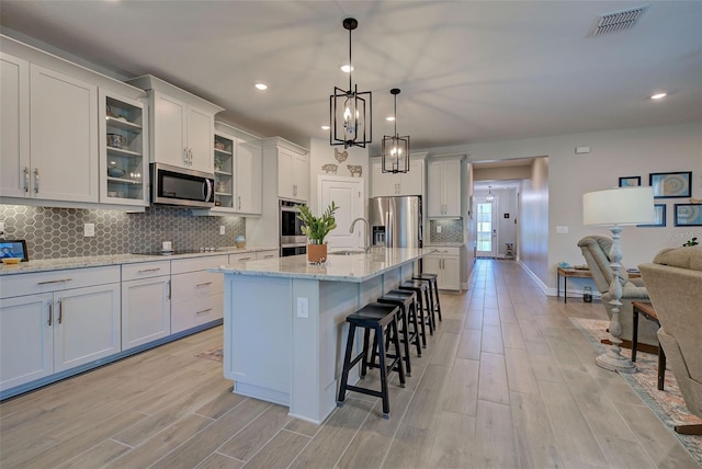 kitchen with white cabinetry, stainless steel appliances, light hardwood / wood-style flooring, a kitchen bar, and a kitchen island with sink