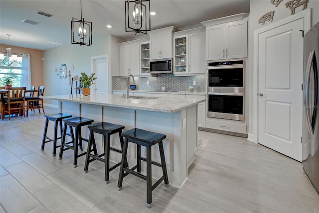 kitchen featuring stainless steel appliances, sink, decorative light fixtures, a center island with sink, and white cabinets